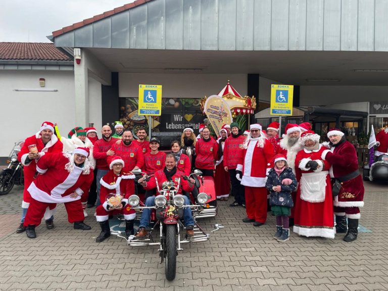 Biker against mobbing e.V. Santa Aktion Gruppe von Weihnachtsmännern und -frauen posiert vor einem Geschäft.