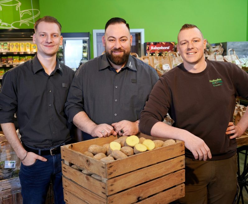 Drei Männer stehen vor einer Kiste mit Kartoffeln in einem Geschäft.