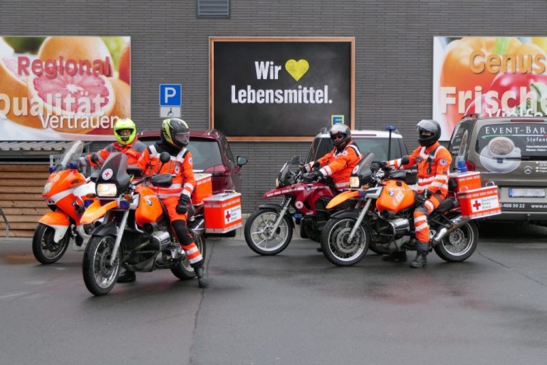 Biker fahren für Kinder - Spende ans PalliativTeam Frankfurt Drei Motorräder mit Fahrern in orangefarbener Uniform vor einem Geschäft. Biker fahren für Kinder Aktion